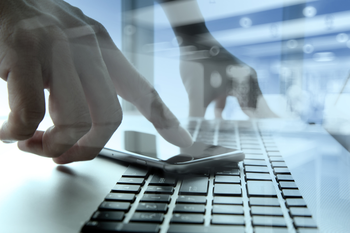 A man pressing his finger onto a phone which is resting on a keyboard